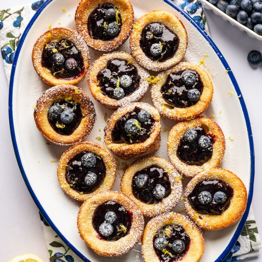 Overhead view of mini dutch baby pancakes on a platter filled with blueberry lemon compote.