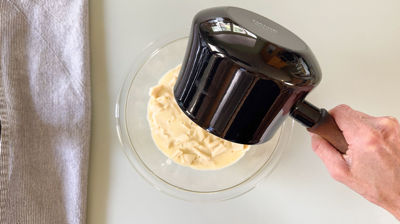 Verser de la crème chaude sur du chocolat blanc haché dans un bol en verre