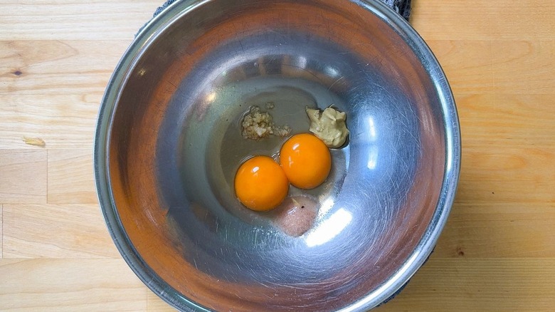 Yoles d'oeufs, sel, ail, moutarde et vinaigre dans un bol en acier inoxydable