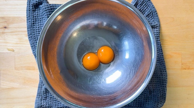 2 jaunes d'oeuf dans un bol en acier inoxydable sur un torchon