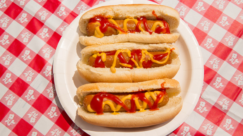 Une vue sur les yeux de trois hot-dogs sur une assiette garnie de moutarde et de ketchup en petits pains