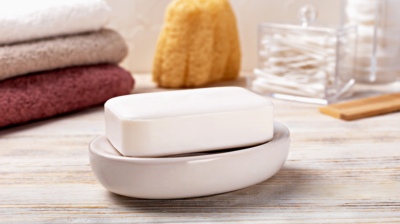 du savon à barres reposant sur un plat avec des serviettes et un pot de Q-tips en arrière-plan
