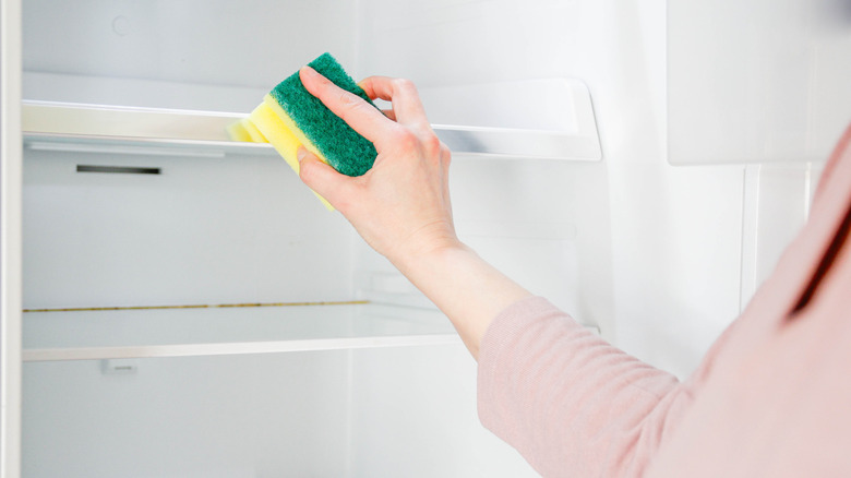 Une femme nettoie l'intérieur d'un réfrigérateur sale