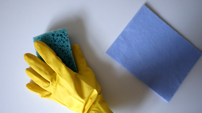 Une main ganée tient une éponge de cuisine à côté d'une lingette réutilisable