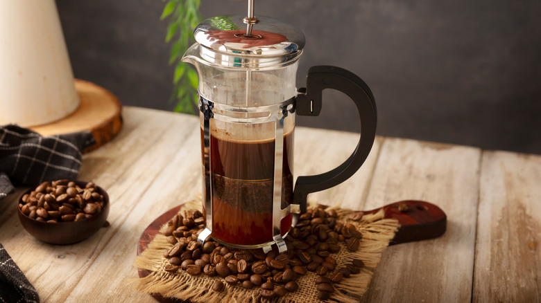 Presse française avec des grains de café à la base au-dessus du comptoir en bois.