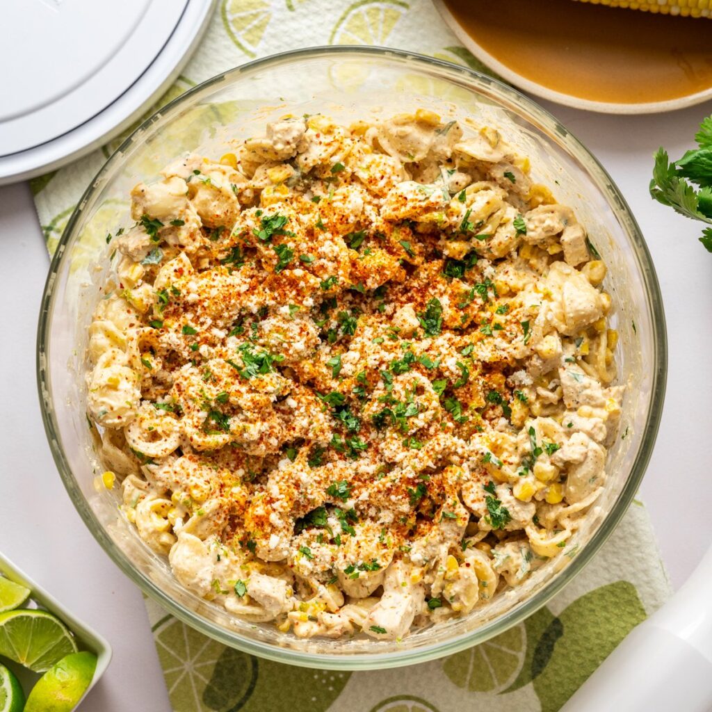 Overhead view of elote pasta salad with grilled chicken in large glass bowl.