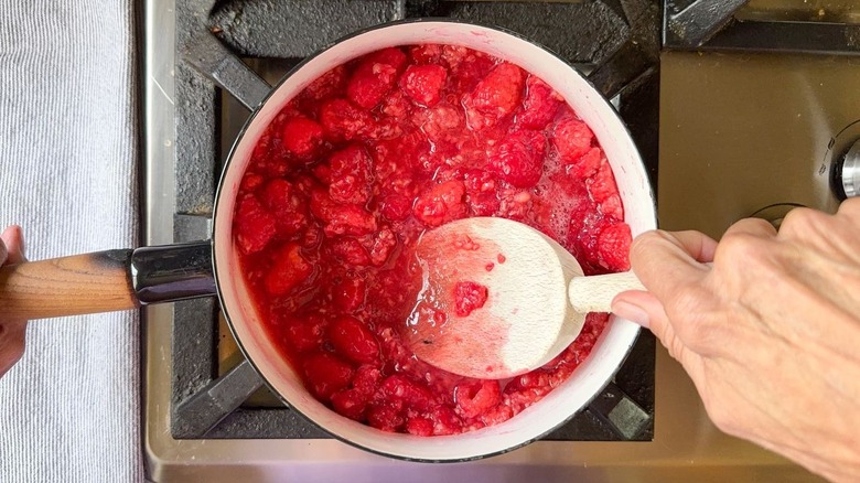 Mercer des framboises fraîches dans une casserole sur la cuisinière avec une cuillère en bois