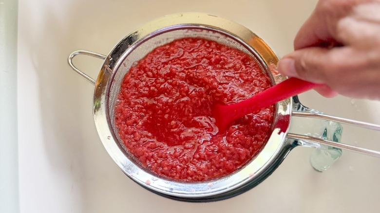Pousser la purée de framboise fraîche à travers une passoire en filet avec spatule