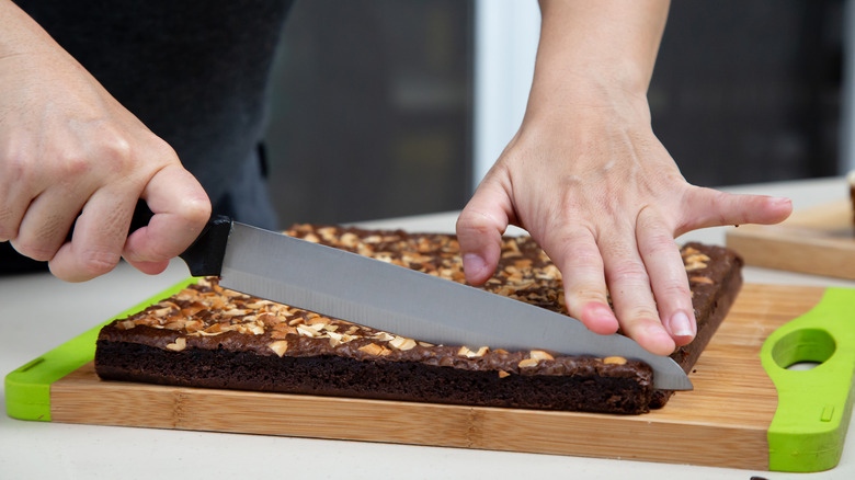 Quelqu'un coupant des brownies sur une planche à découper en bois
