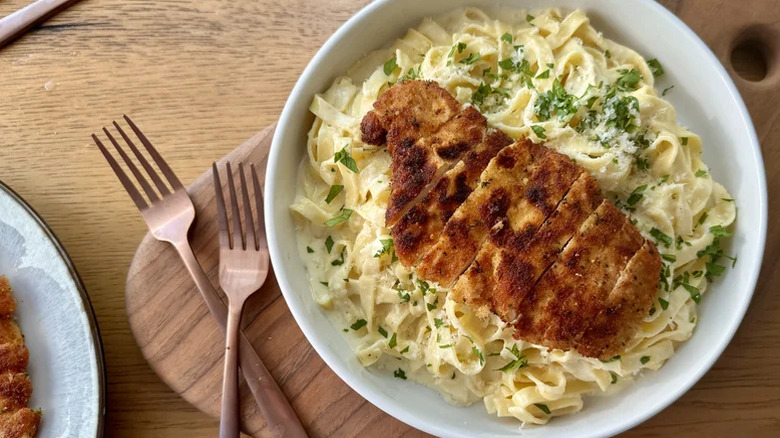 Bol blanc de fettucine crémeuse alfredo avec poitrine de poulet panée en tranches sur le dessus