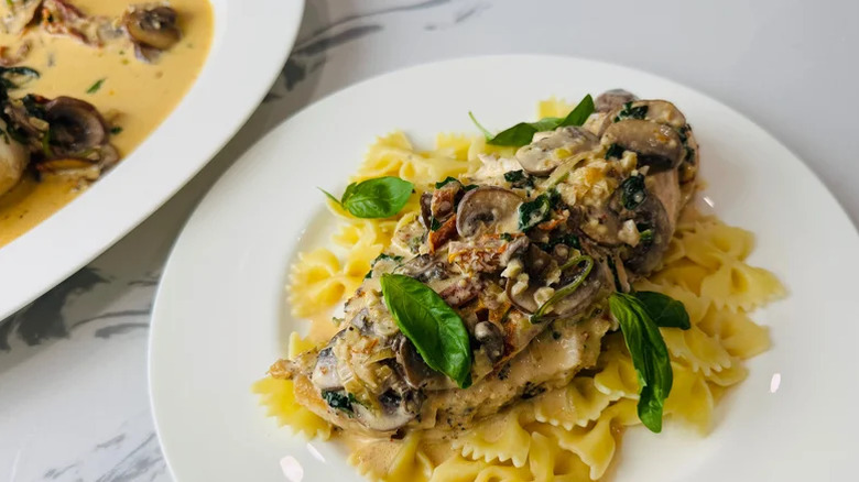 Assiette blanche de poitrine de poulet avec tomate séchée au soleil, épinards et sauce aux champignons sur un lit de farfalle