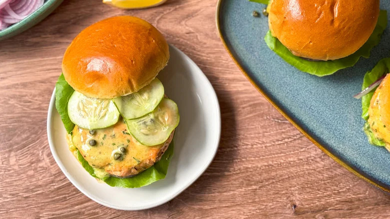 Assiette blanche avec un hamburger de saumon sur un petit pain garni de concombre en tranches, de laitue et de sauce remoulade au curry