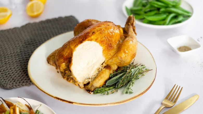Assiette blanche avec du poulet rôti entier avec une tranche de viande de poitrine coupée garnie d'herbes fraîches