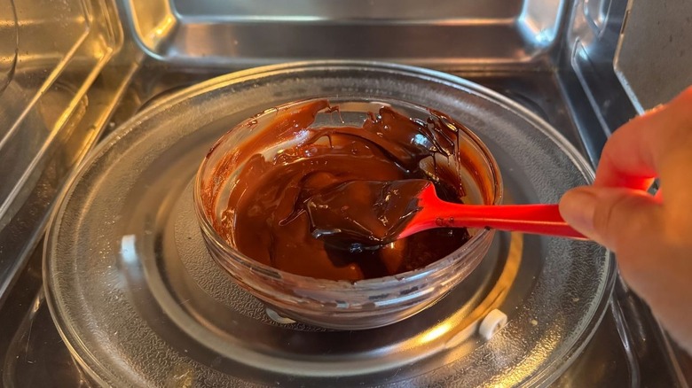 Inclination de chocolat fondu dans un bol en verre au micro-ondes avec spatule en caoutchouc