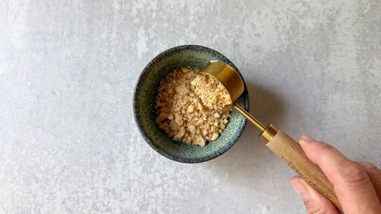 Ajout de noisettes hachées dans un petit bol avec une cuillère à soupe