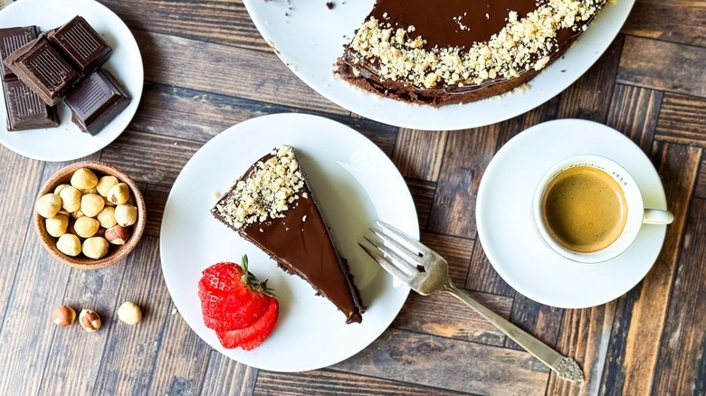 Gâteau de chocolat italien Gianduja italien sans farine en tranches dans l'assiette avec des noisettes, du chocolat, une garniture aux fraises et un expresso