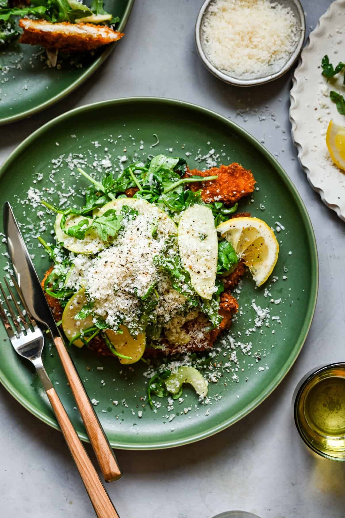 Vue aérienne de la escalope de poulet garnie de roquette et de salade de pomme rasée et de parmesan râpé.