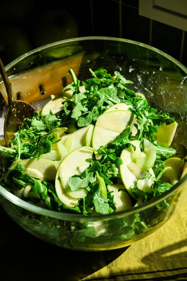 Salade de pomme, de céleri et de roquette dans un bol en verre.