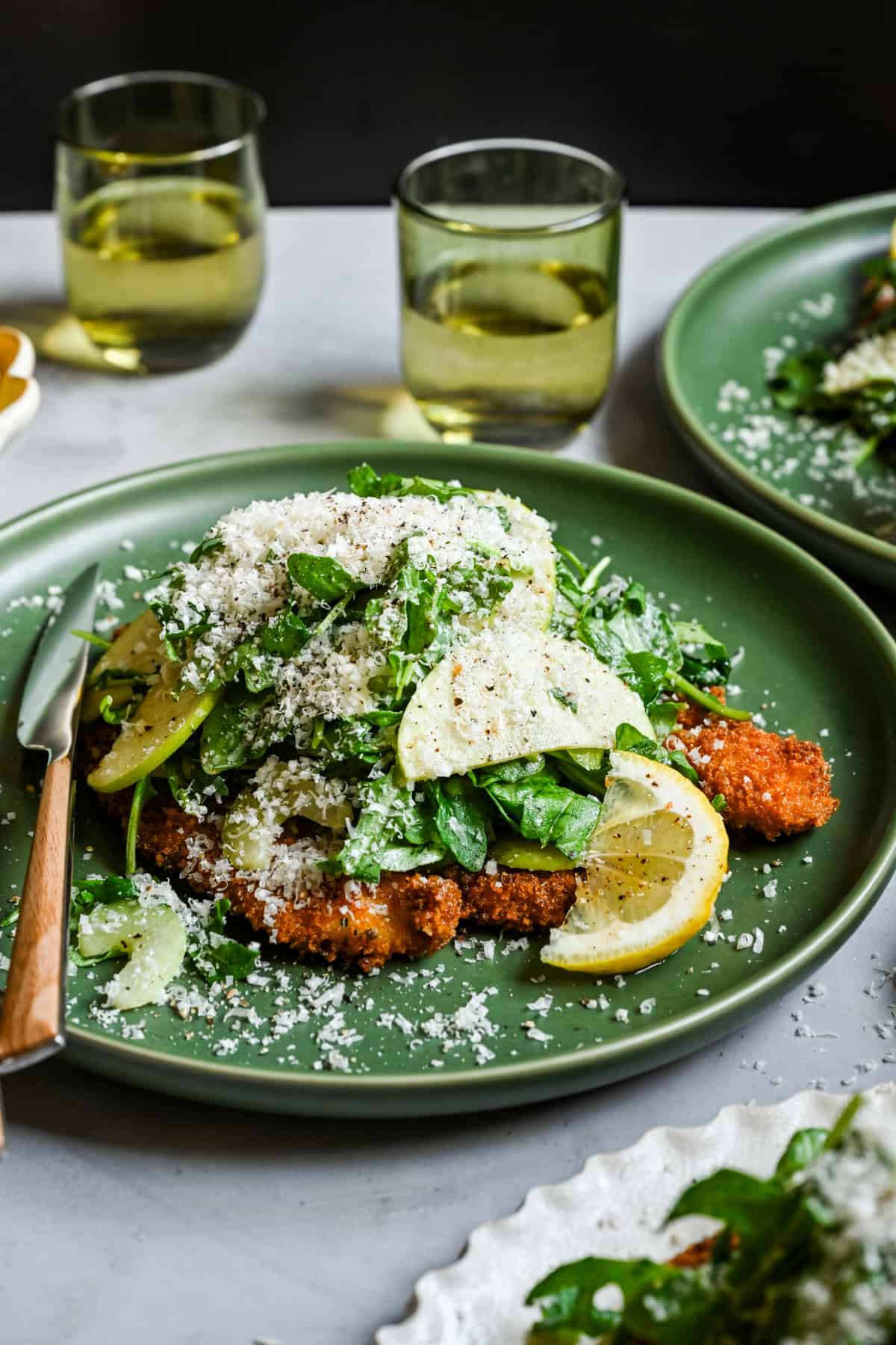 Vue latérale de la jardin de poulet garnie de roquette et de salade de pomme rasée et de parmesan râpé.