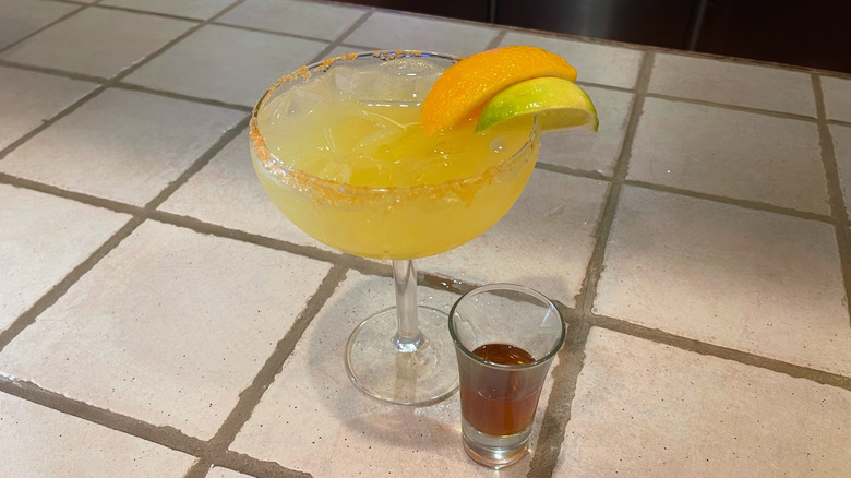 La Margarita italienne d'Olive Garden sur un bar blanc avec une garniture de citron vert et d'orange et un shot d'Amaretto à côté