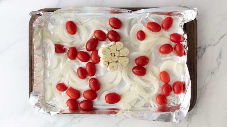 Tomates cerises, oignons émincés et tête d'ail sur une plaque à pâtisserie