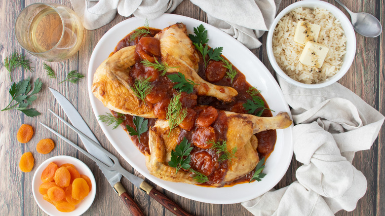 poulet dans une sauce brun rougeâtre aux herbes vertes sur une assiette blanche