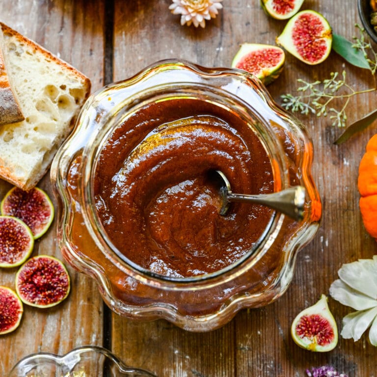 Confiture de figues sucrées dans un pot en verre sur une table rustique en bois avec du pain, des figues fraîches et des fleurs.