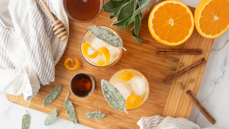 cocktails pâles de couleur orange avec de la glace, des feuilles de sauge et des écorces d'orange
