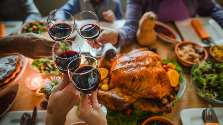 Une table de Thanksgiving présente une dinde tandis que les mains des gens trinquent avec du vin rouge au-dessus de l'oiseau.
