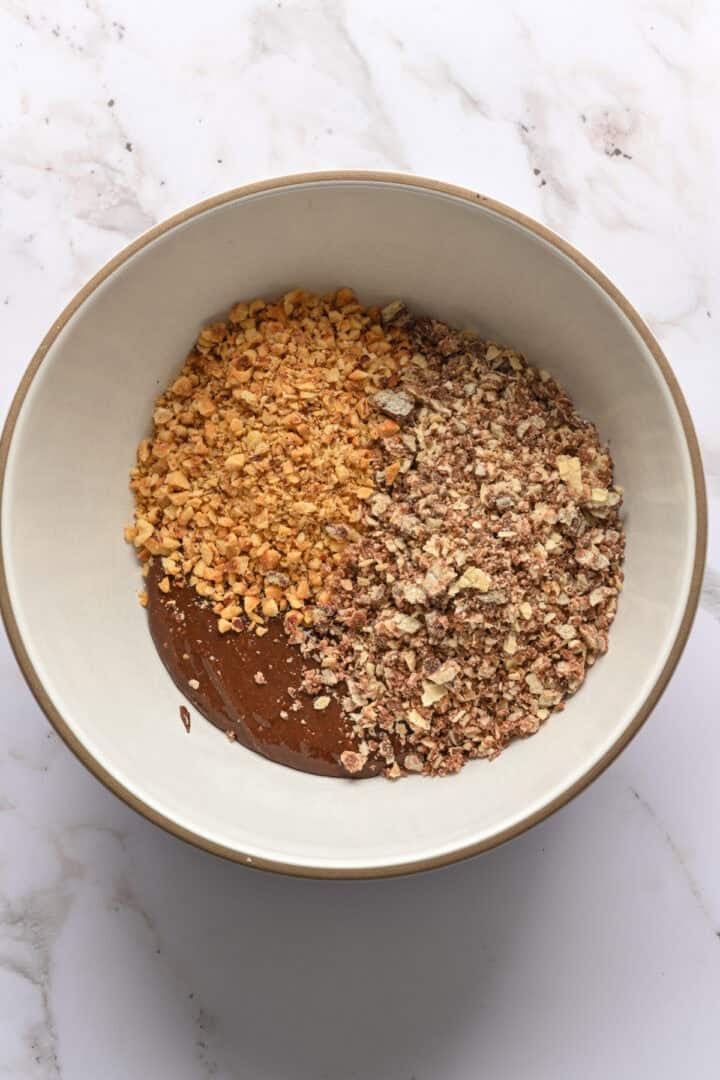 Vue aérienne du nutella, des biscuits gaufrés hachés et des noisettes hachées dans un bol avant de mélanger.