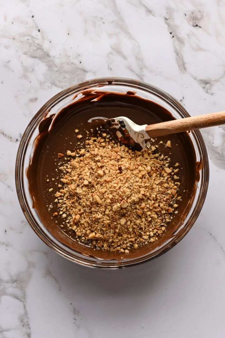 Chocolat fondu et noisettes hachées dans un bol avant de mélanger.