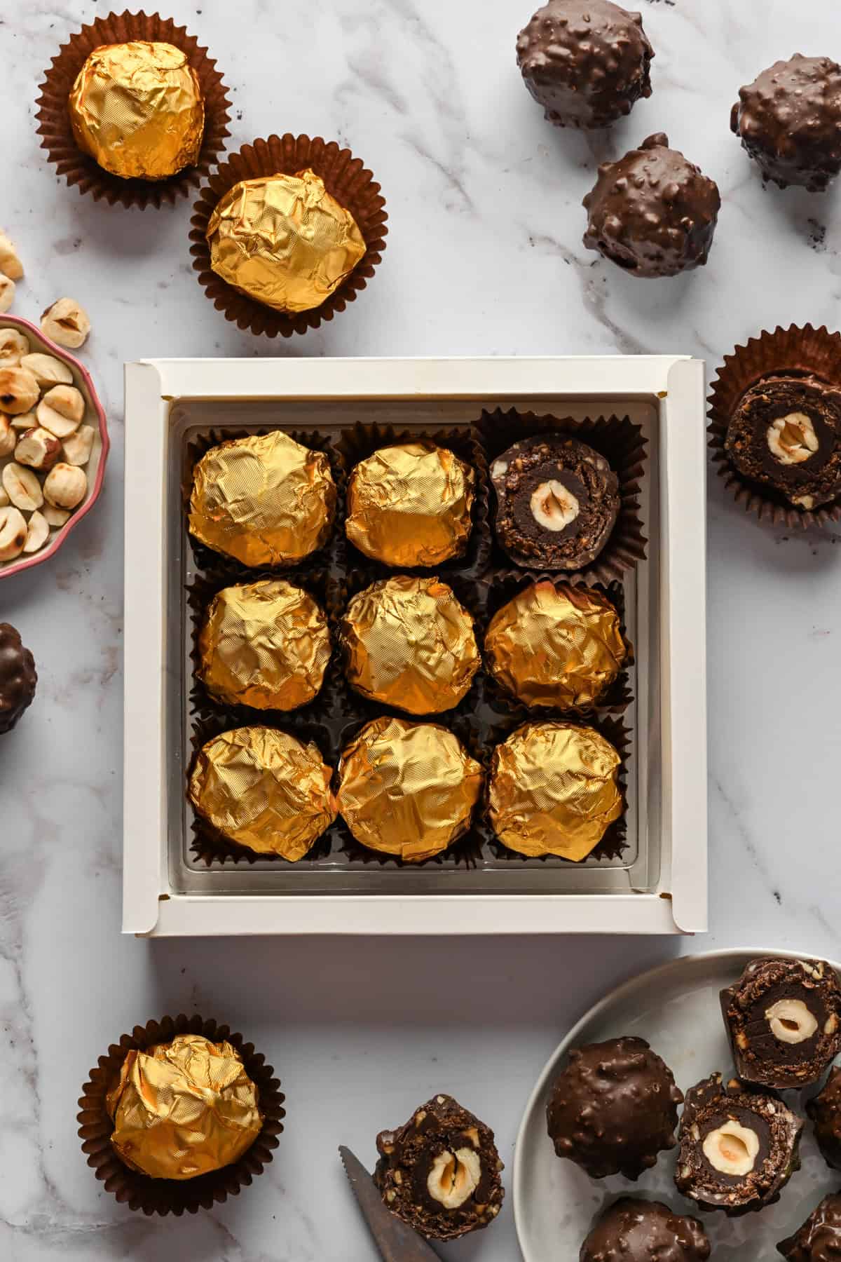 Vue aérienne de truffes ferrero rocher faites maison enveloppées dans une feuille d'or dans une boîte cadeau avec quelques truffes non emballées autour de la boîte.