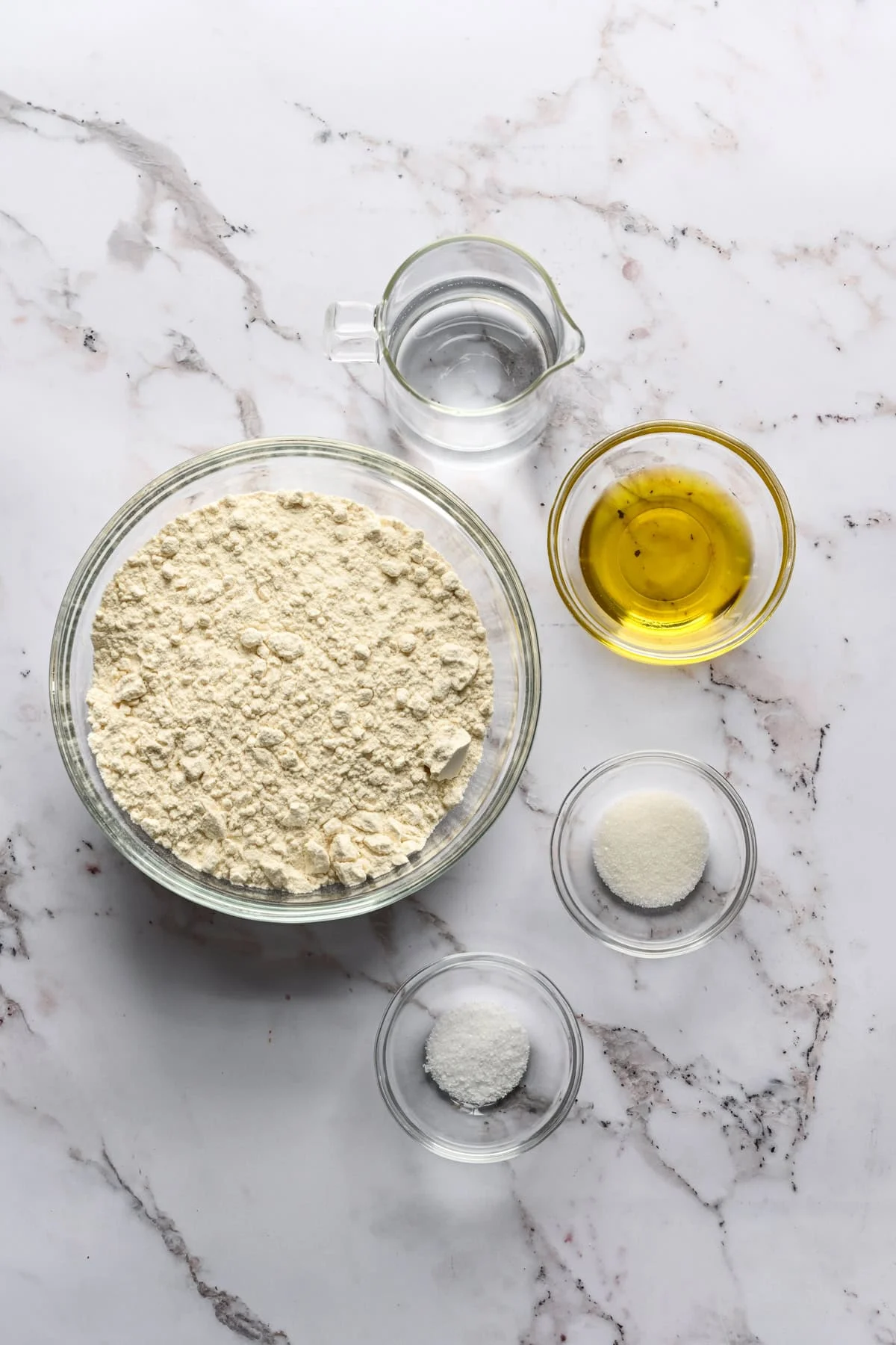 vue aérienne de la farine, de l'eau, de l'huile d'olive, du sel et du sucre dans des bols.