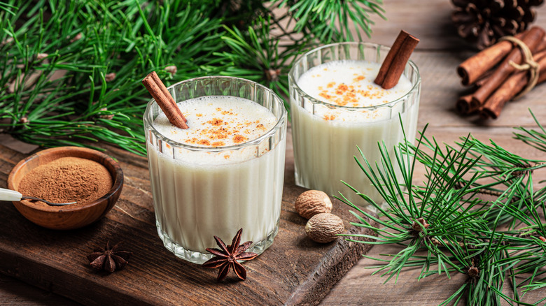 Deux verres de lait de poule avec des bâtons de cannelle entourés de branches d'arbre de Noël