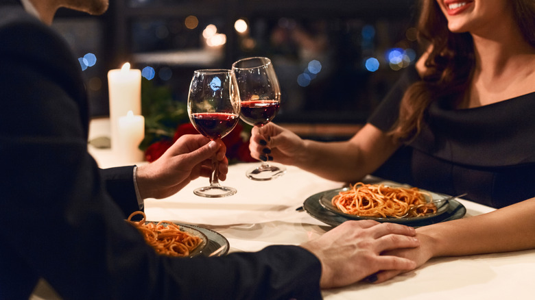 Un couple grillant des verres à vin sur des assiettes de spaghetti dans un restaurant