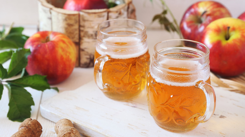 Deux verres de cidre de pomme pétillant à côté des pommes.