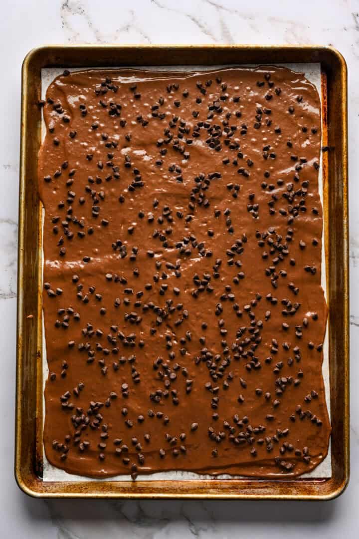 Brownie cassant sur une plaque à pâtisserie, étalé sur un morceau de papier sulfurisé.