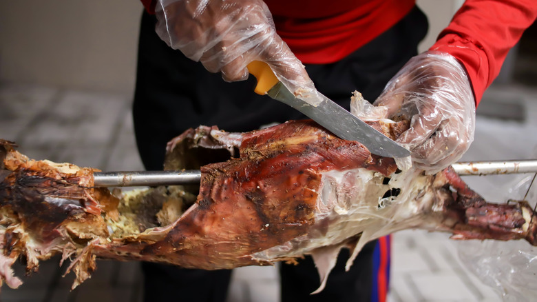 un homme coupant une chèvre grillée sur un rôtissoire à la broche