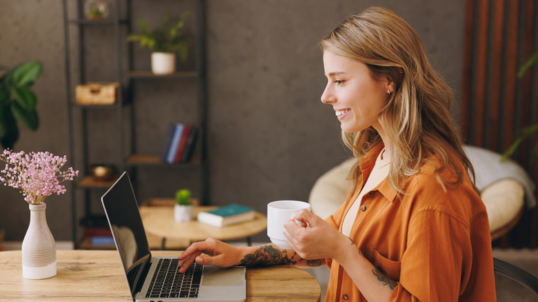 Femme buvant du café en tapant sur un ordinateur portable.