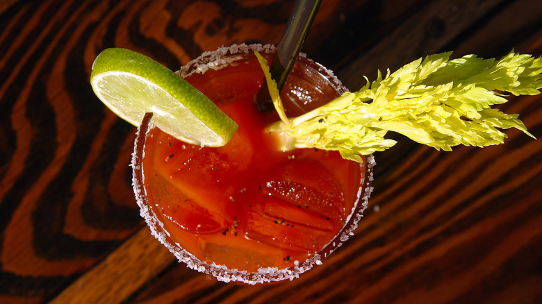 Cocktail Bloody Mary garni de céleri, de gombo, d'oignon, d'olive et de sel sur une table rustique en bois. Un Bloody Mary est un cocktail contenant de la vodka, du jus de tomate et d'autres épices.