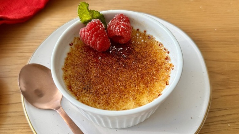 Une crème brûlée dans un ramequin blanc garnie de framboises et d'une feuille de menthe.