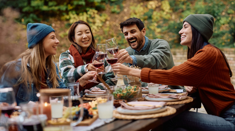 Quatre personnes trinquant avec du vin sur une longue table de pique-nique en plein air.