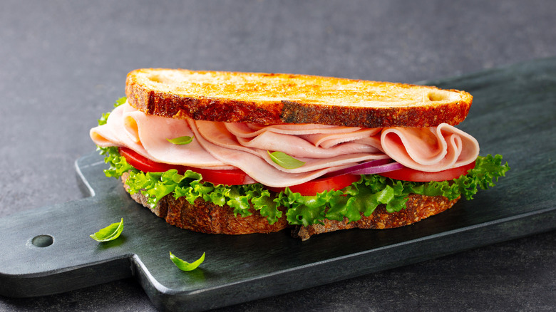 Sandwich au jambon, tomate et laitue sur une planche à découper grise