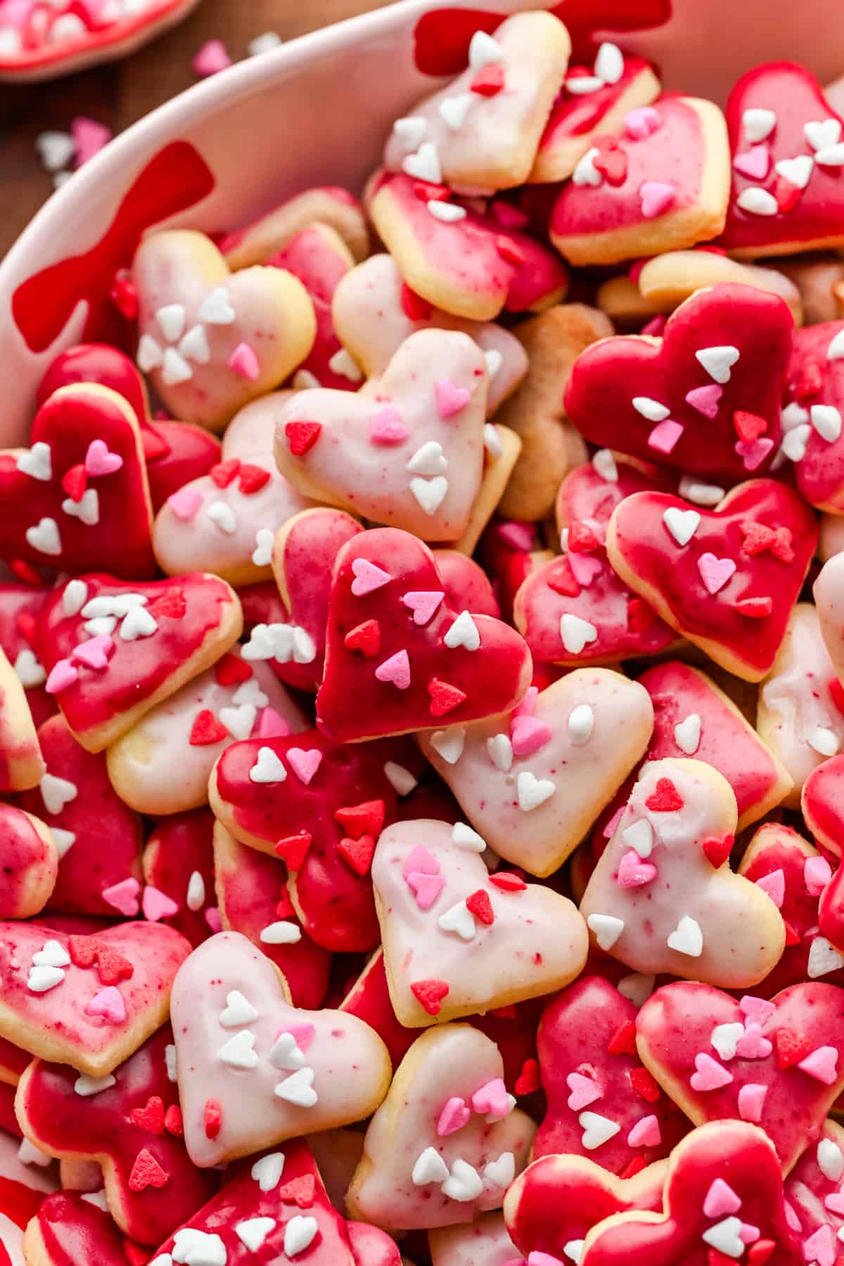Vue rapprochée de mini biscuits coeur avec glaçage rose et pépites de coeur dans un bol rose.