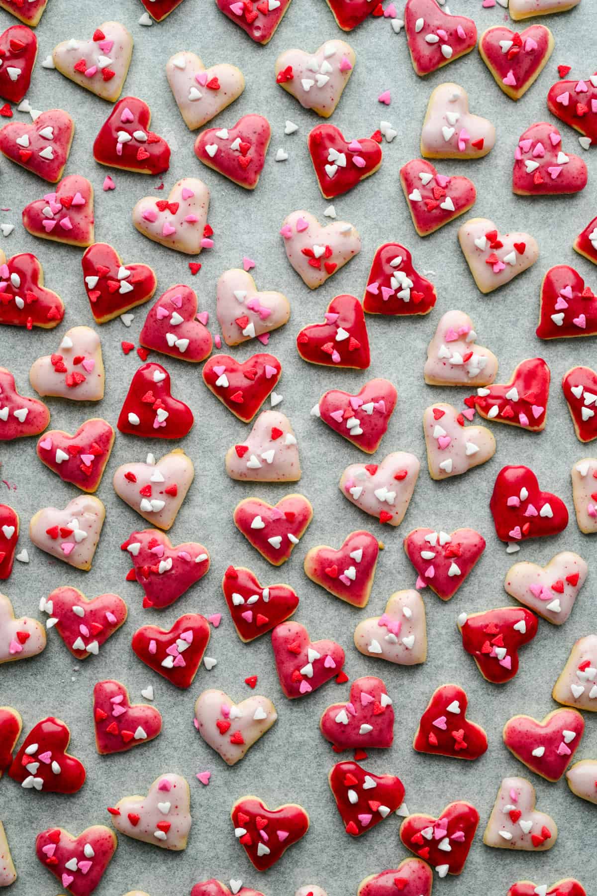 Vue aérienne de mini biscuits coeur avec glaçage rose et pépites de coeur sur papier parchemin.