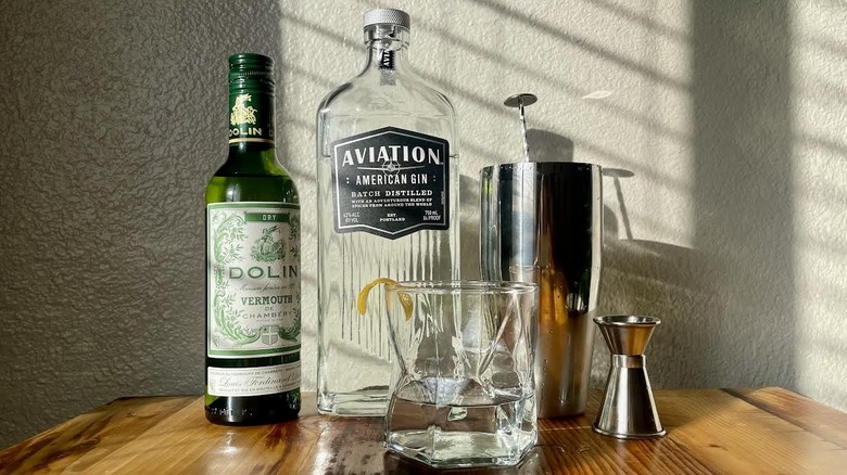 Une bouteille de Dolin Dry Vermouth, Aviation Gin et du matériel de fabrication de martini.
