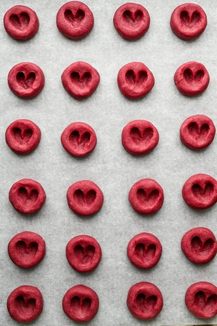 Biscuits à empreinte de cœur aux framboises sur une plaque de cuisson avant de les remplir de confiture.