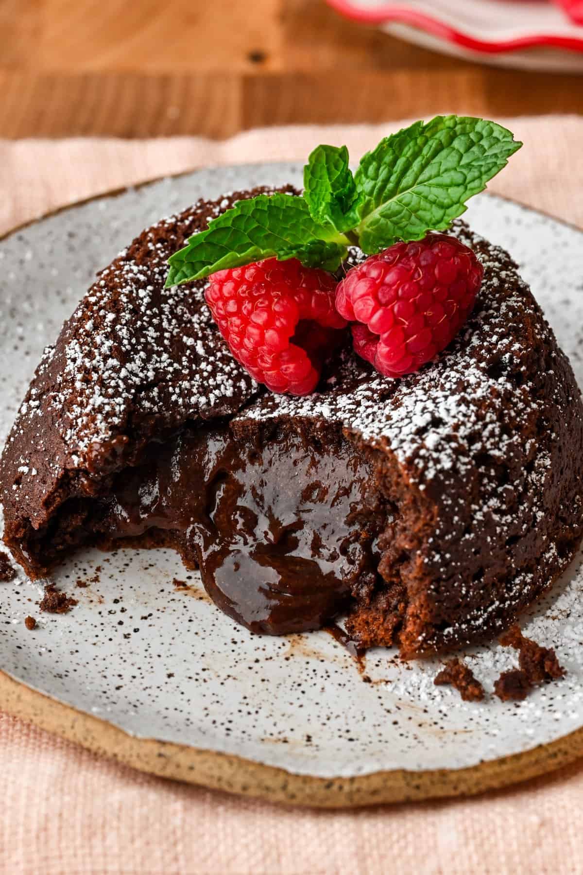 Vue rapprochée du gâteau de lave au chocolat sur une assiette avec un centre fondu qui coule, garni de framboises et de menthe.