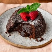 Vue rapprochée du gâteau de lave au chocolat sur une assiette avec un centre fondu qui coule, garni de framboises et de menthe.