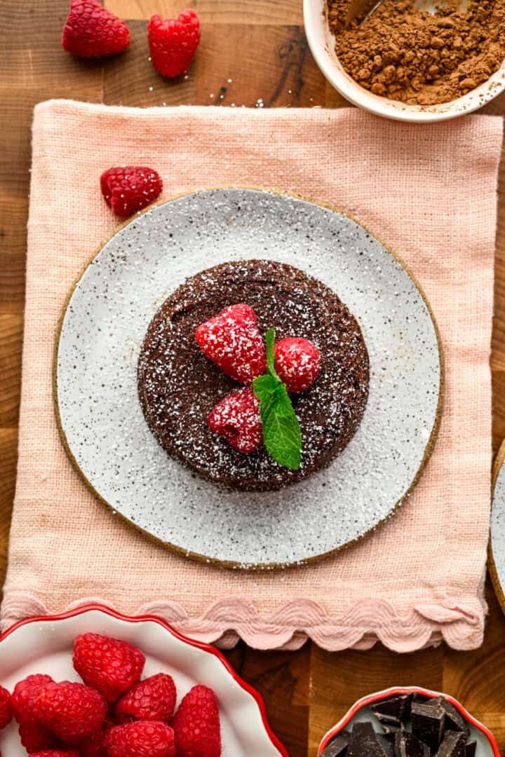 Gâteau de lave au chocolat cuit au four sur une petite assiette blanche garnie de framboises et de menthe.